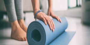 what are the benefits of yoga? - woman rolling out a yoga mat, with bare feet and leggings on.