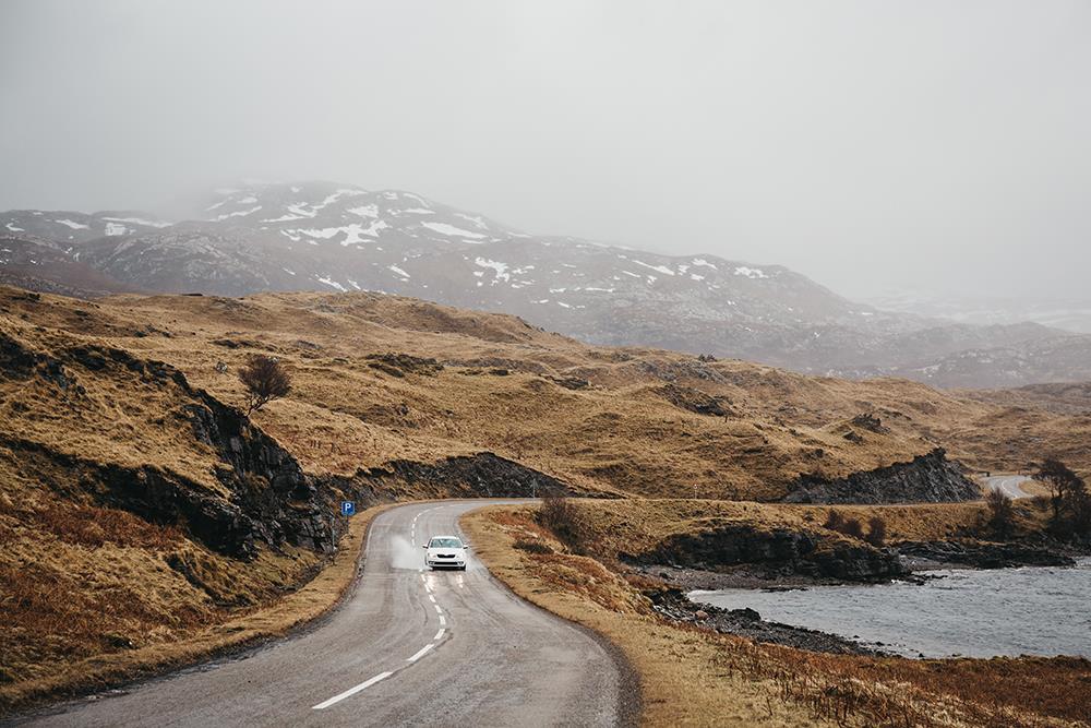 Unidentified car driving on a road going through Scottish Highlands
