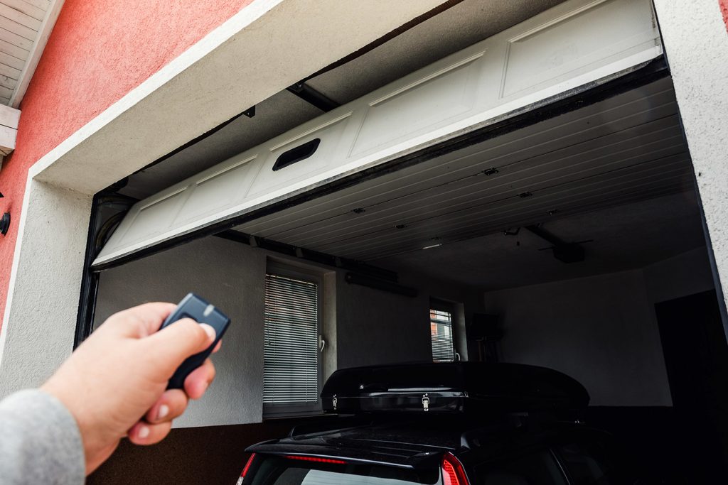 Car theft on the rise, but you can stop it! - A man is clicking a button held in his hand to close his garage with his car inside