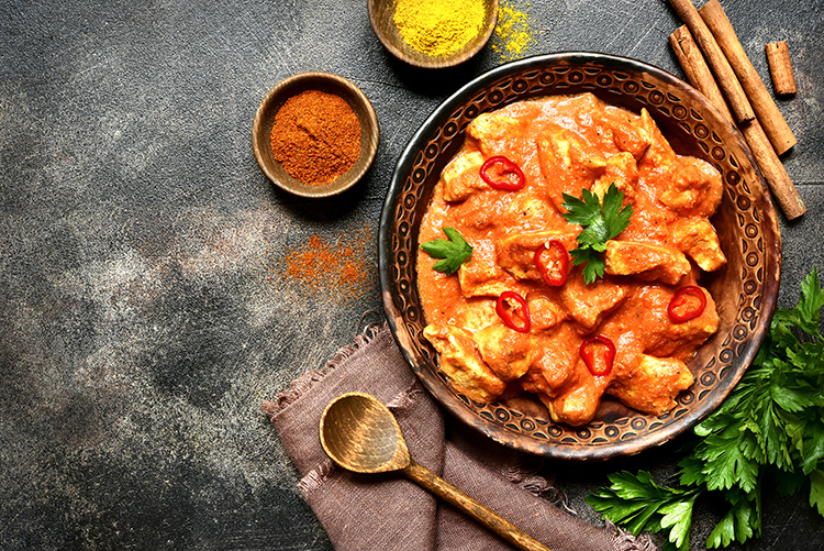 8 Benefits of Spicy Foods - a bowl of curry with two bowls of spices, fresh coriander and a wooden spoon.