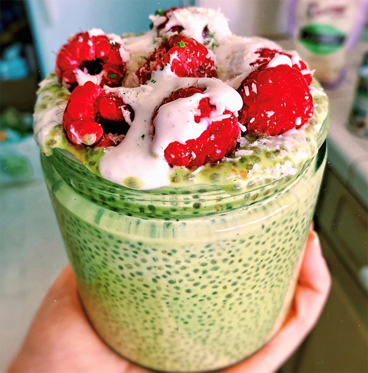 A green smoothie with raspberries and pin yoghurt on top being held up in a kitchen