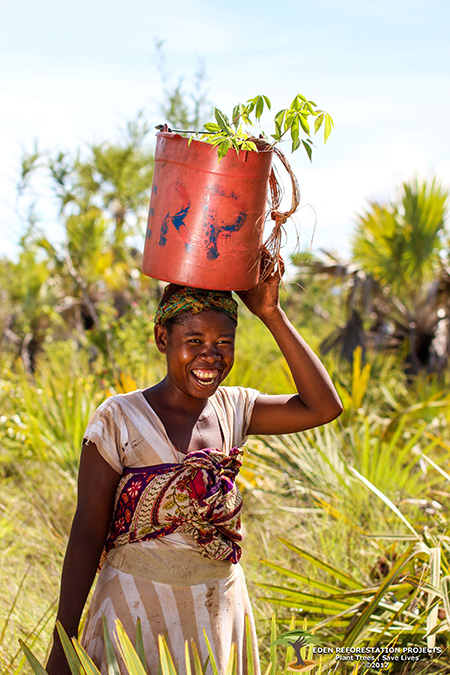 Celebrating 333 million trees planted - a girl is laughing, balancing a red bucket on her head in a field of trees. She is dressed in traditional clothes.