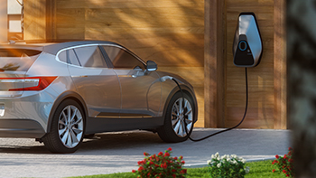 5 things to think about when buying an electric vehicle. A silver car being charged outside a house with wooden cladding.