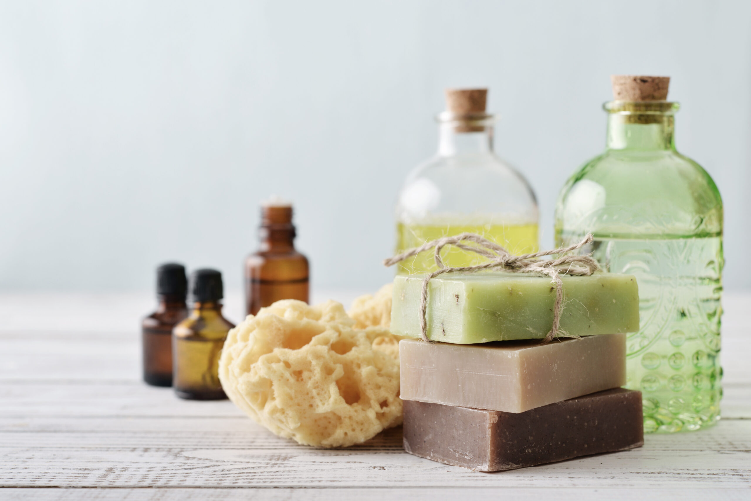 5 Sustainable Household Swaps to Make Today. Stack of soap bars with sponge and bottles on light background