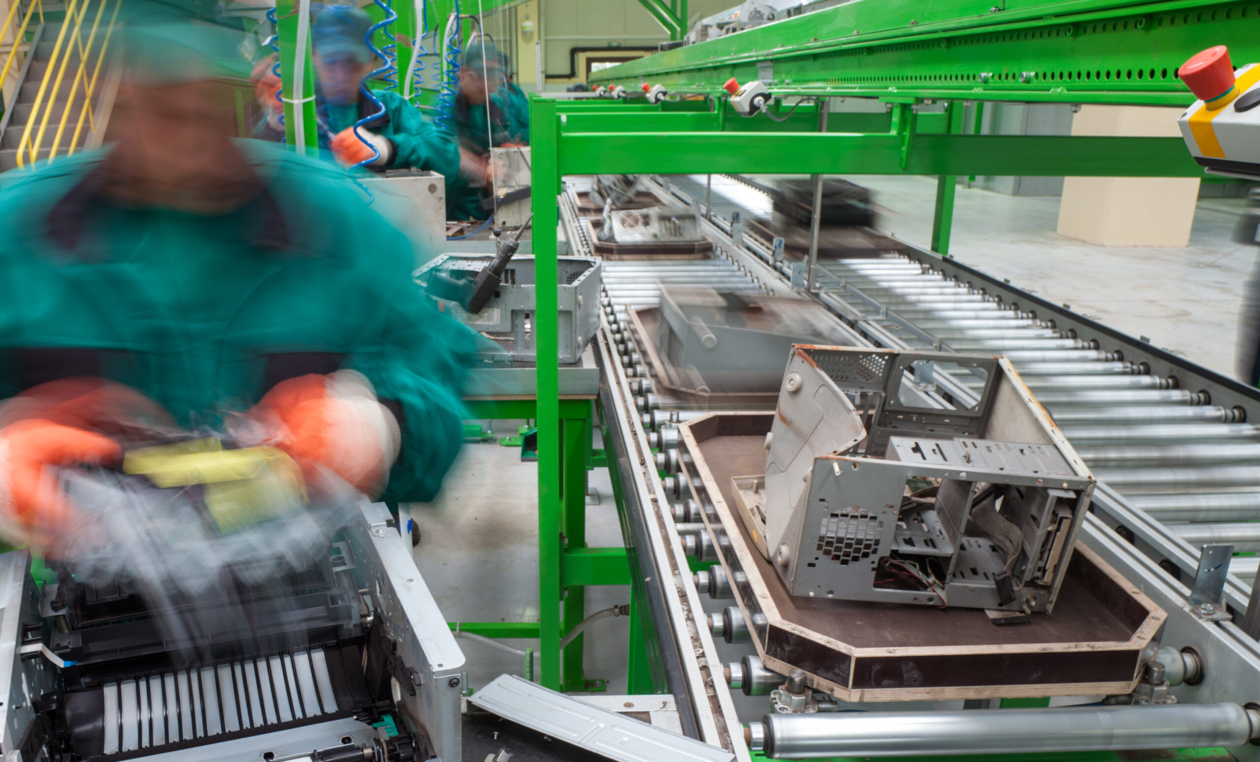 Blurred figures of workers in a disassembling plant are disposing old computer electronics.