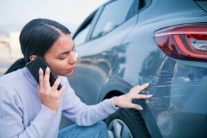 A woman inspecting a scratch on the back of her car whilst on the phone