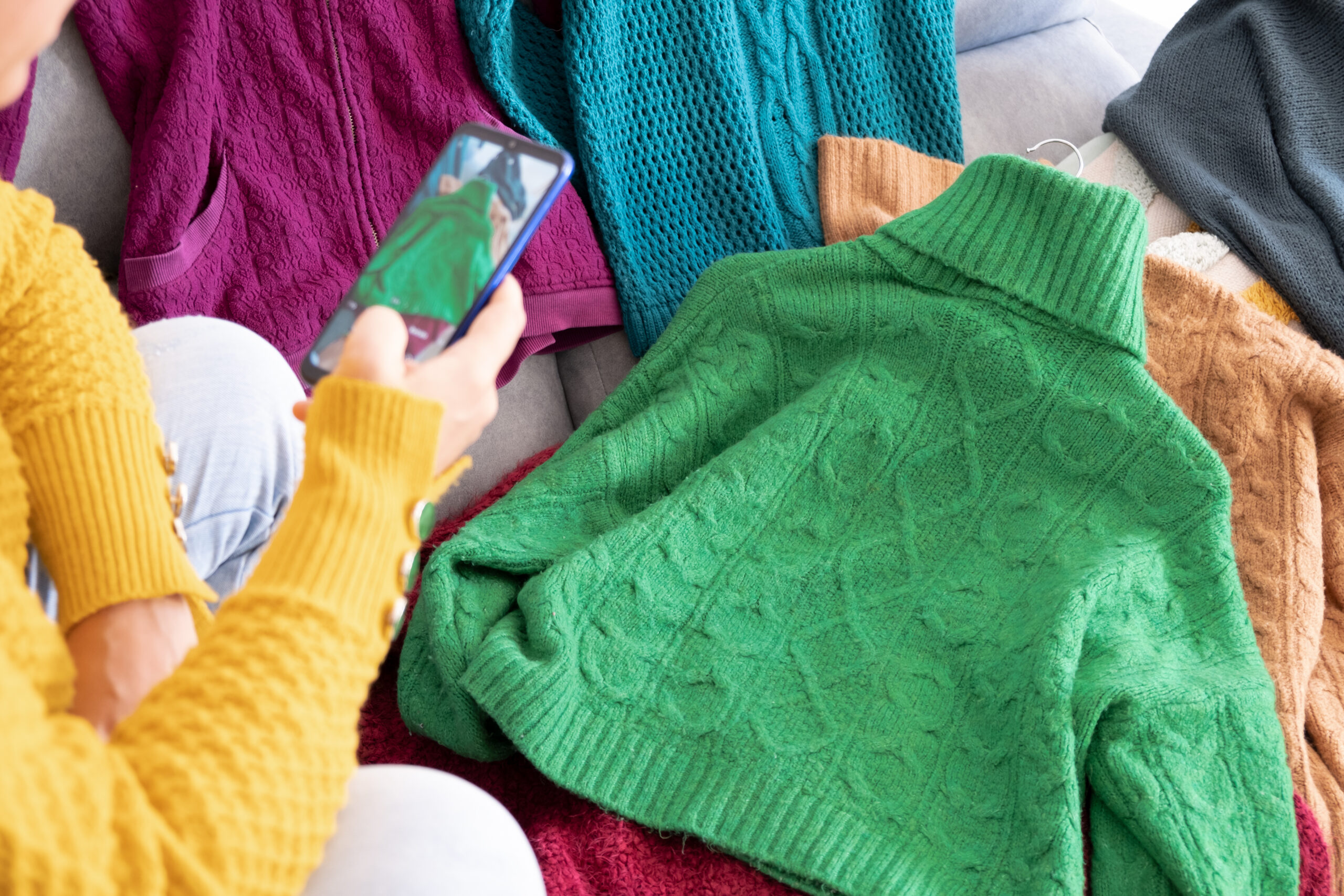 woman with phone in hand, taking photo of green jumper to sell second