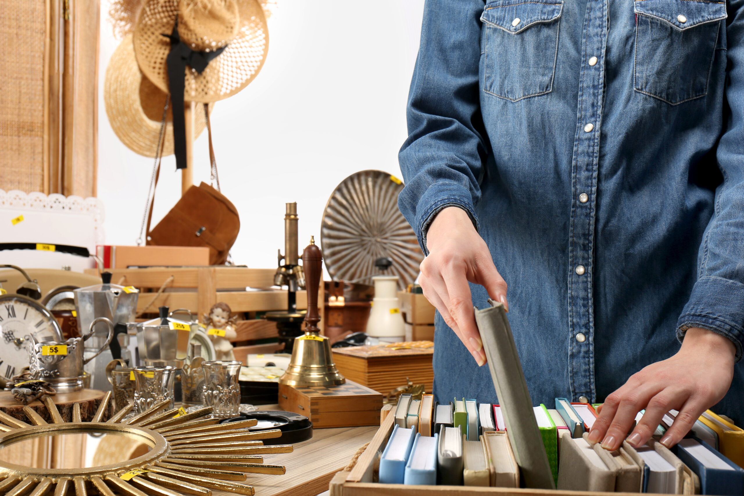 Woman choosing book near table with different stuff indoors, closeup. Garage sale