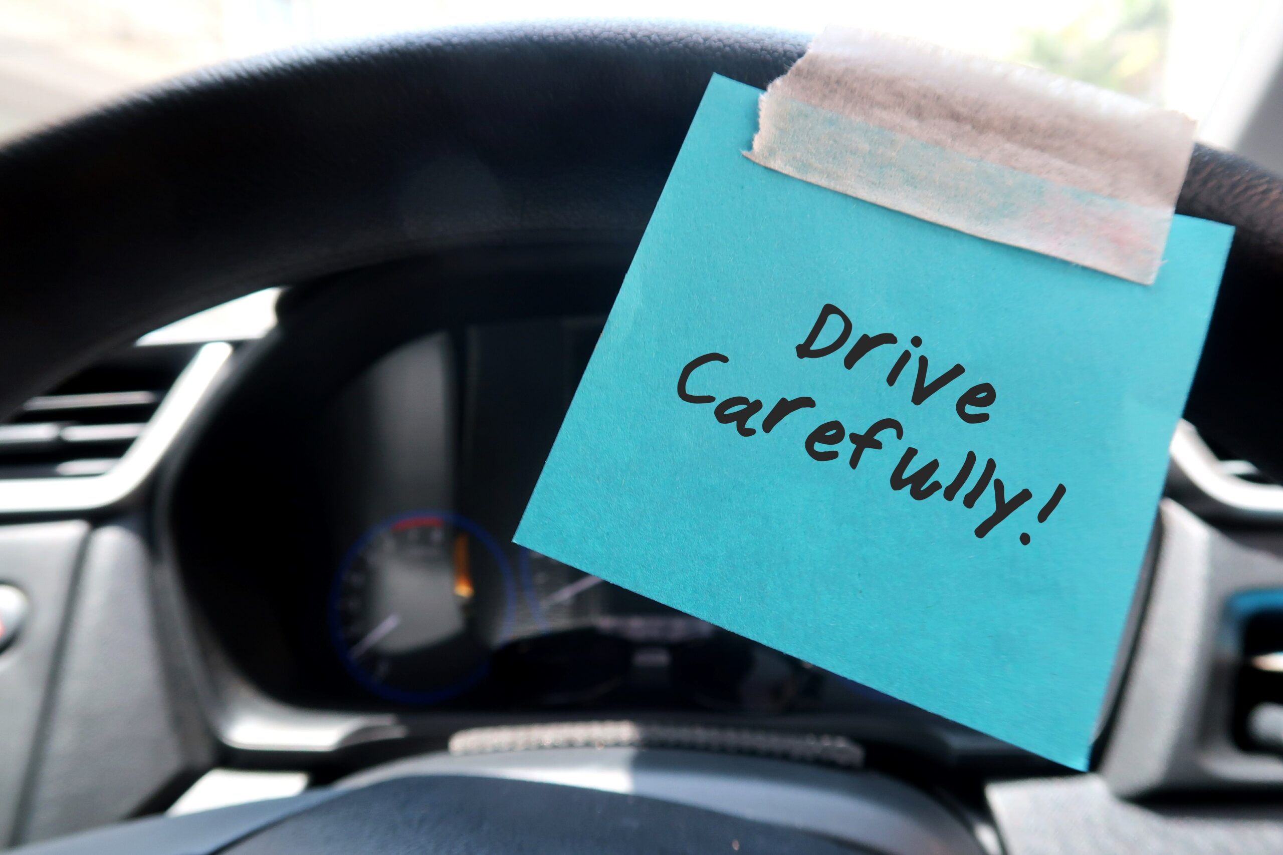 Post it note on steering wheel reminding driver to 'Drive Carefully'