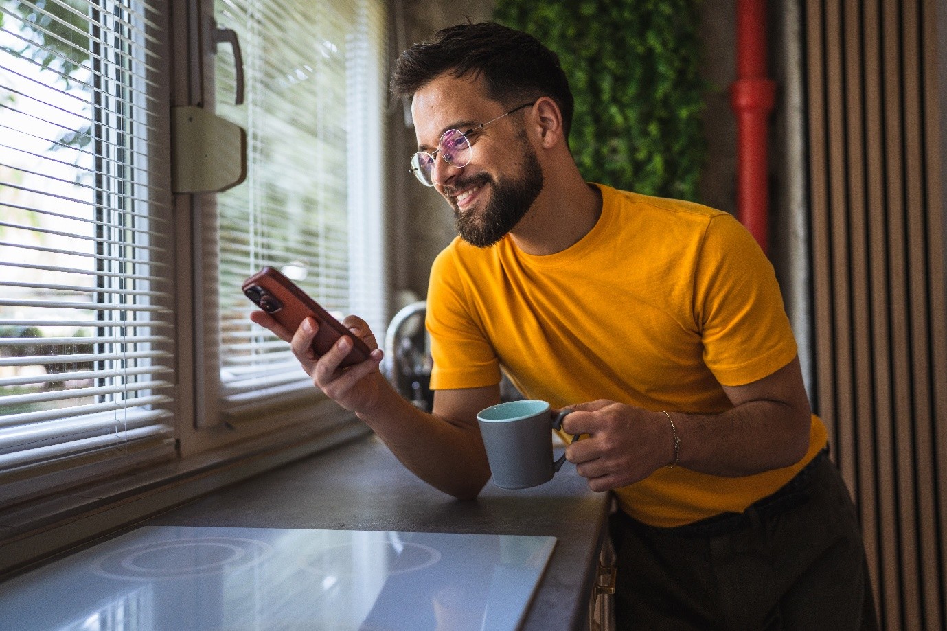Male scrolling through phone, smiling with a mug of tea/coffee